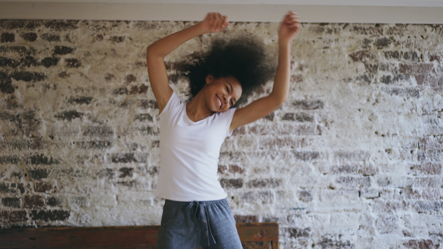 Femme qui danse joyeusement les bras levés dans une pièce lumineuse