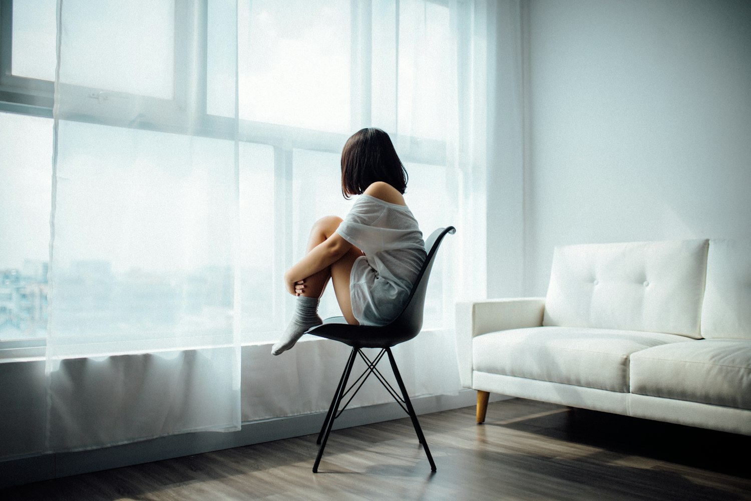 Femme recroquevillée sur une chaise près d une fenêtre dans une lumière feutrée